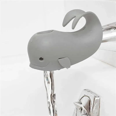 Grey whale-shaped bath spout cover designed for baby safety, fitted on a faucet with water flowing out.