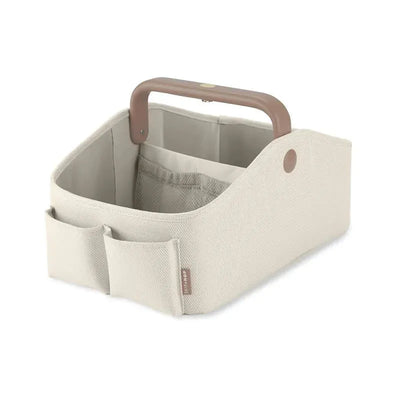 Light beige Skip Hop diaper caddy with a brown handle, featuring multiple compartments for organizing baby essentials.