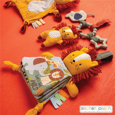Soft book featuring a lion design with colorful ribbons, surrounded by plush animal toys, on a bright orange surface.