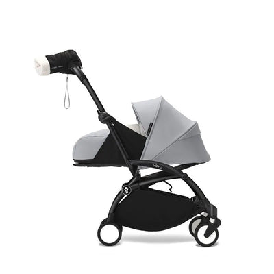 Black Babyzen™ Yoyo mittens attached to the handle of a grey stroller, designed for warmth and comfort.