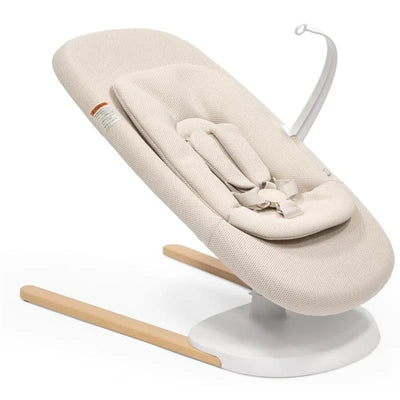 Yoga™ Baby Bouncer in Light Sand by Stokke, featuring a soft fabric seat, safety harness, and wood legs.