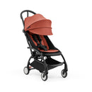 Compact stroller with a black frame and berry-colored seat, featuring adjustable canopy and harness system.