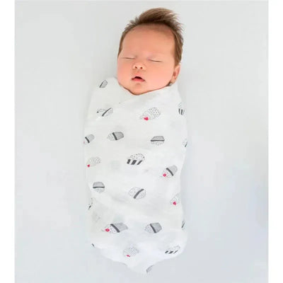 Swaddle Designs Black & White Cupcakes Marquisette Swaddle Blanket wraps a sleeping baby, featuring a cupcake pattern.