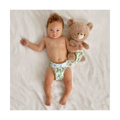 Infant wearing a Swaddle Designs Honest Cotton Muslin Hybrid reusable diaper cover with a cactus pattern, holding a teddy bear.