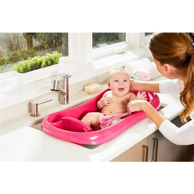 Baby enjoying bath time in a pink tub with a sling, while a caregiver gently supports and interacts with them.