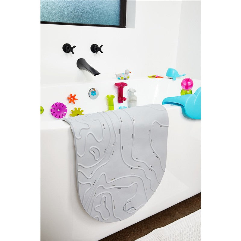 Boon GRIFFLE bathtub mat in gray draped over the side of a white tub, surrounded by colorful bath toys.