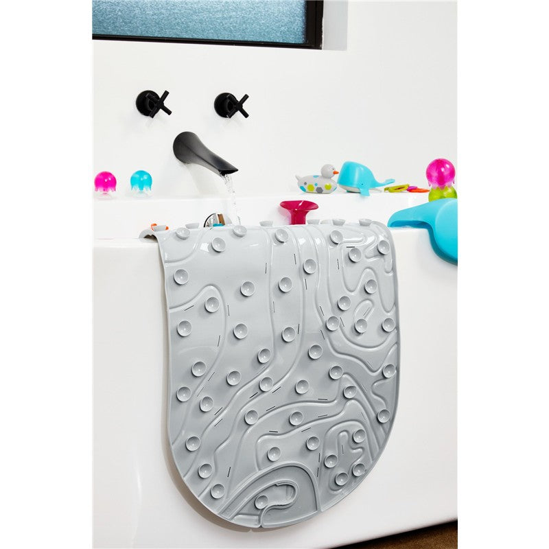 Gray Boon GRIFFLE bathtub mat with a textured surface hanging over the edge of a bathtub, surrounded by colorful bath toys.