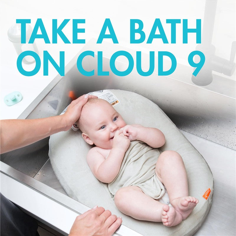 Boon PUFF+ Inflatable Baby Bather with a cheerful baby in a sink, enjoying bath time while being gently supported by a hand.