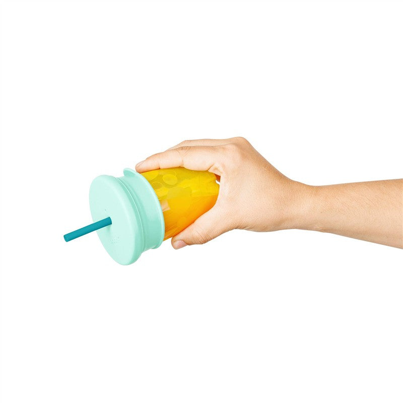 Boon SNUG Silicone Straw Lid in green attached to a cup held by a hand, with yellow liquid inside.