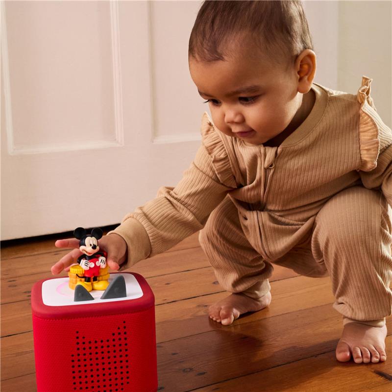 Child in a beige outfit interacts with a red Tonies audio toy featuring a Mickey Mouse figurine.