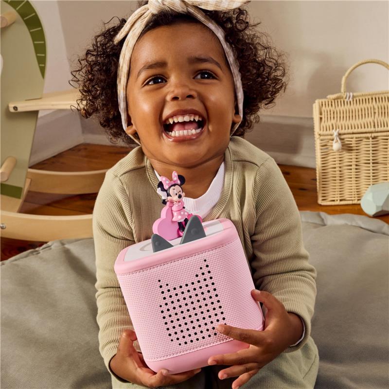 Child smiling while holding a pink Minnie Mouse audio toy figurine, featuring a speaker and playful design.