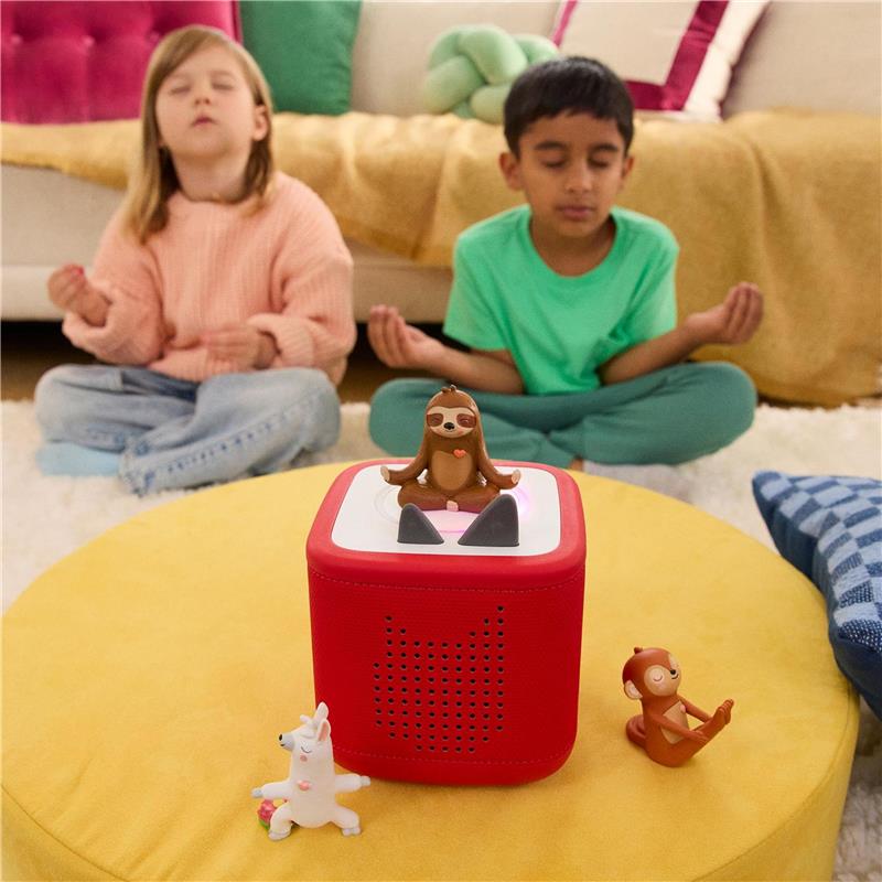Children meditating with closed eyes, seated on a rug, next to the Tonies audio toy featuring a sloth figurine.
