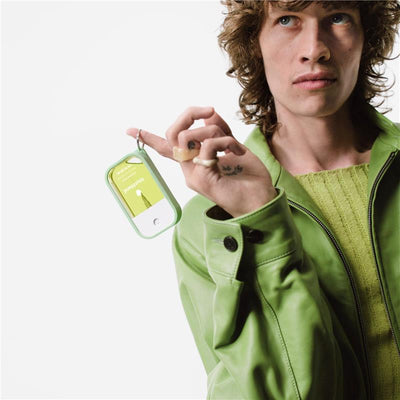 Touchland Hand Sanitizer Mist in a green silicone case with keyring held by a person in a green jacket.