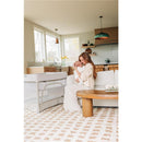 Mother holding a newborn in a cozy living room with a UPPAbaby Remi V2 Playard nearby.