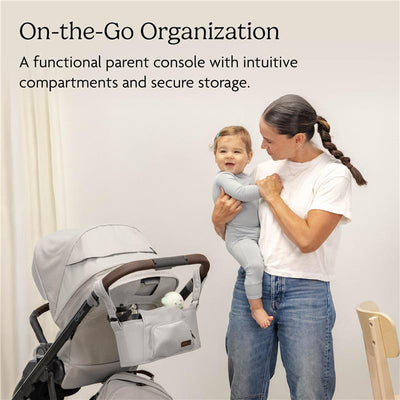 Light grey UPPAbaby Carry-All Parent Organizer attached to a stroller, with a woman holding a young child nearby.