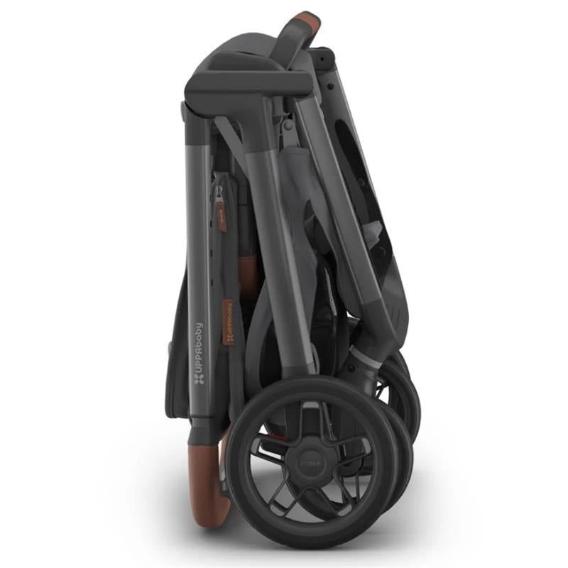 Uppababy Kona stroller in a folded position, showcasing its graphite fabric and brown leatherette handle.