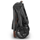 Uppababy Kona stroller in a folded position, showcasing its graphite fabric and brown leatherette handle.