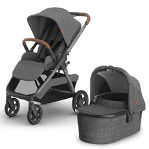 Uppababy Kona Stroller in graphite color with brown leatherette handlebar and a matching bassinet, both featuring a modern design.