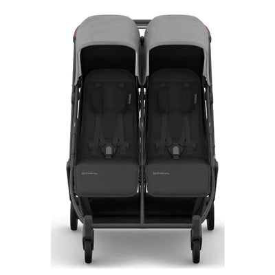 Compact double stroller with two side-by-side seats, charcoal fabric, carbon frame, and saddle leather accents.