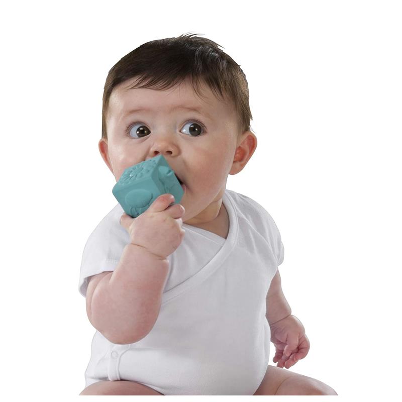 Baby in a white onesie holds a blue Vulli Sophie La Girafe So’Pure cube, exploring it by mouth.