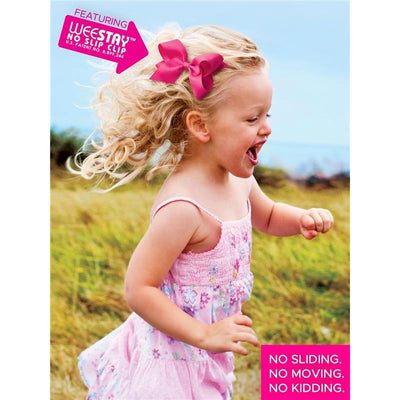 Child with curly blonde hair wearing a pink dress and a large pink grosgrain bow, playing joyfully outdoors.