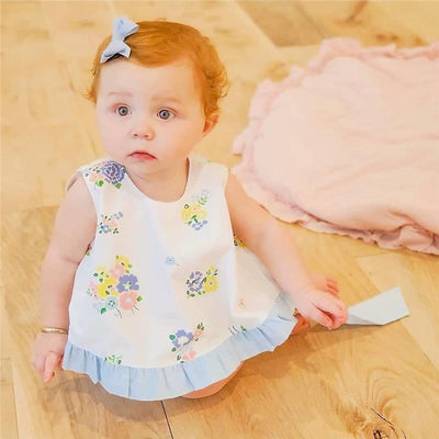 Baby girl with curly red hair and a tiny blue grosgrain hair bow, wearing a floral dress, sitting on a wooden floor.