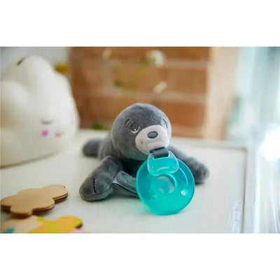 Soft gray seal plush with a teal pacifier attached, surrounded by colorful toys on a white surface.