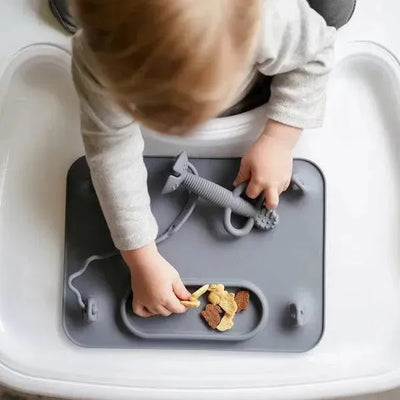 Baby using a grey Busy Baby Mat silicone placemat with snacks and a toy in a high chair