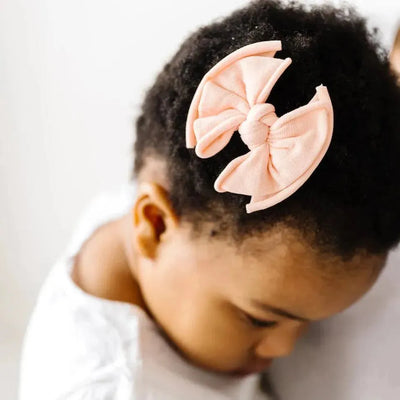 Close-up of a baby wearing a peach-colored Baby Bling Bows fabric hair clip.