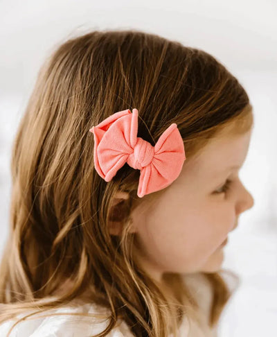 Young girl wearing a coral Baby Bling Bows fabric hair clip in her brown hair.