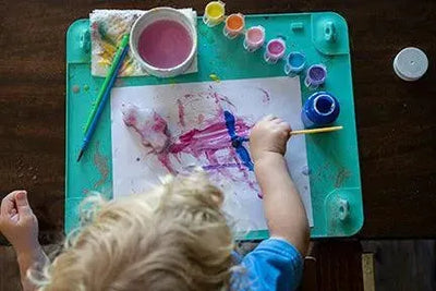 Toddler using Busy Baby Mat paints and brushes for creative art play.