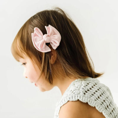 A young child wearing a pink Baby Bling Bows fabric hair clip in her brown hair.